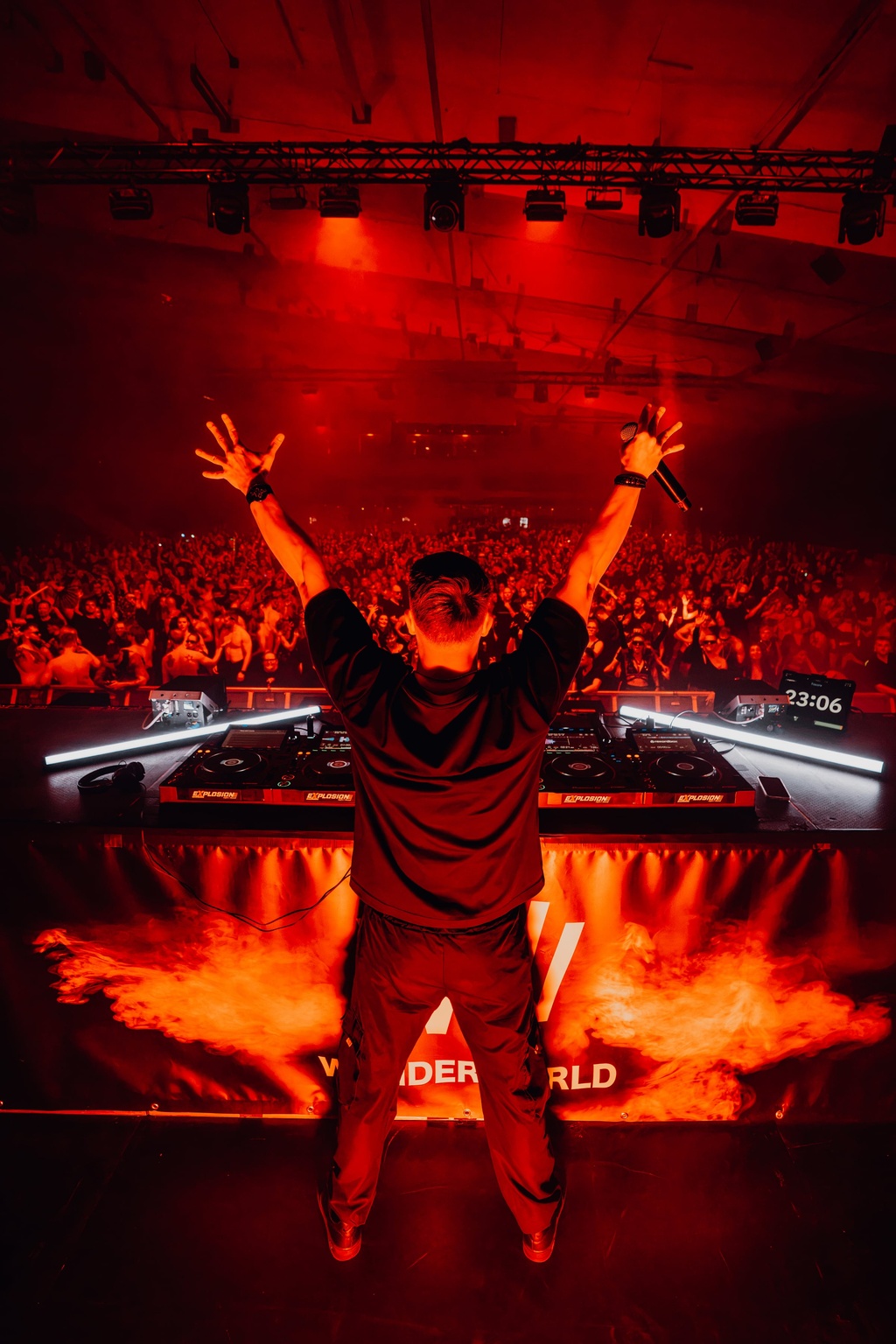 TISCORE seen from behind with arms wide open in a red lit arena.