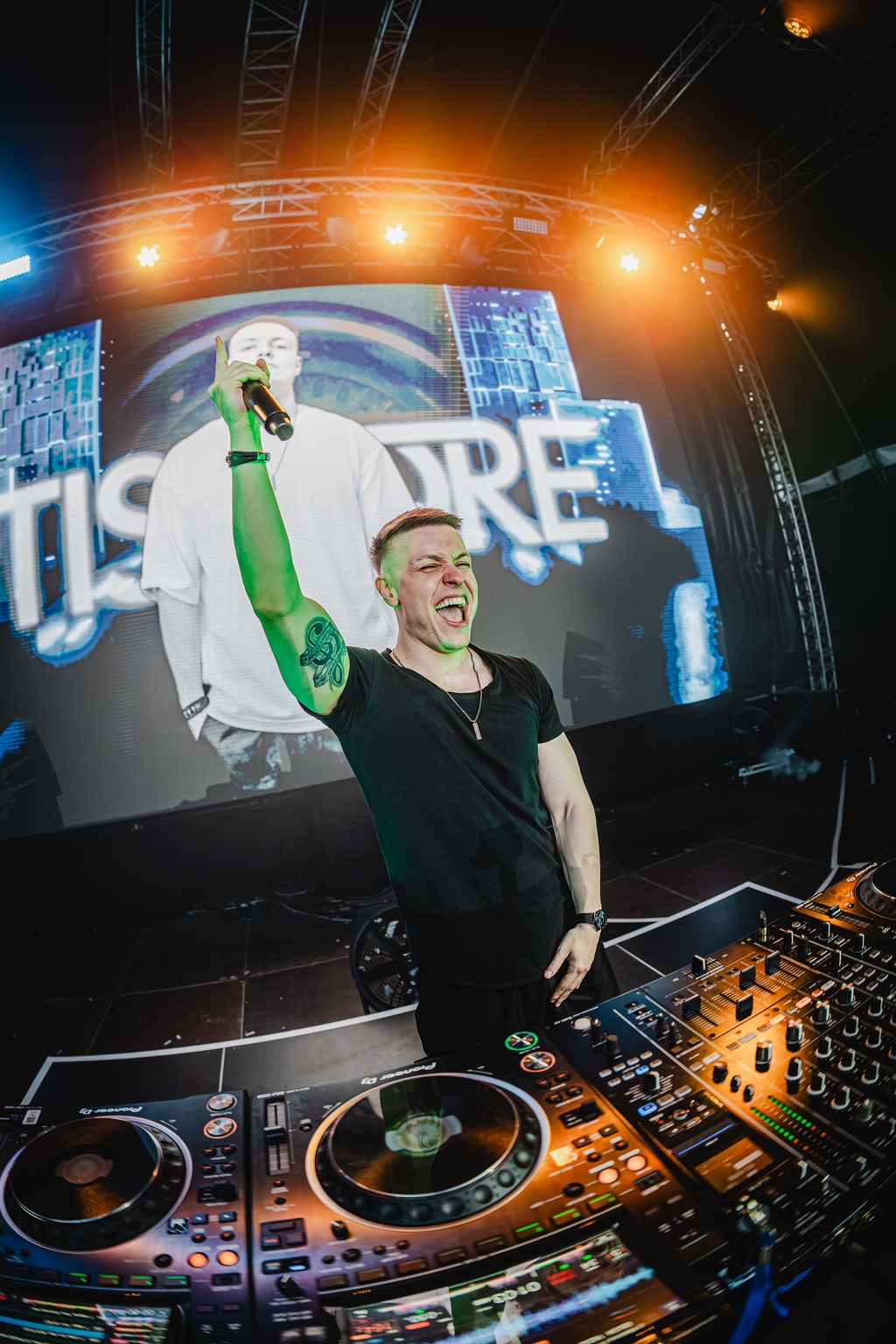 TISCORE raising his arms at the decks while his name fills the stage screen.